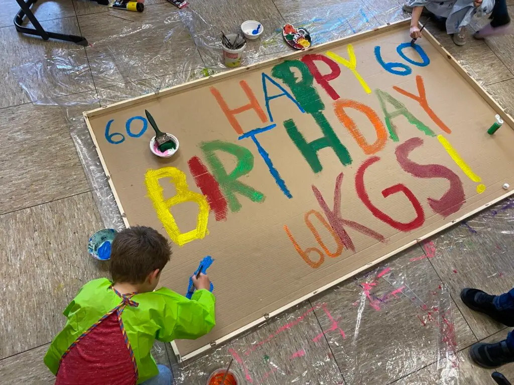 Kinder malen Happy Birthday KGS mit Farbe auf ein Plakat.