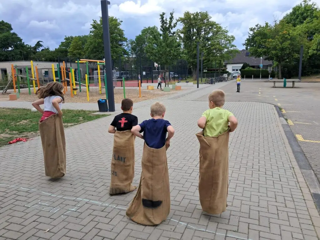 Kinder veranstalten ein Sackhüpfen auf dem Schulhof.